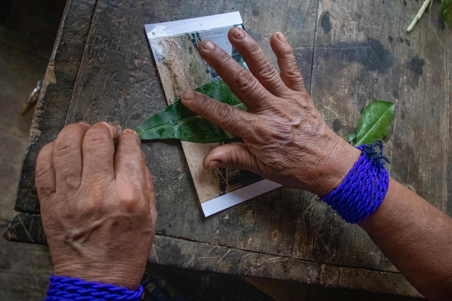 Rogelina Arce, guérisseuse traditionnelle, guérit symboliquement une photographie de la rue principale de son village, Puesto Indio, à l'aide de feuille de calebassier. Cette rue a été le lieu d'une récente incursion de la part d'un groupe armé.